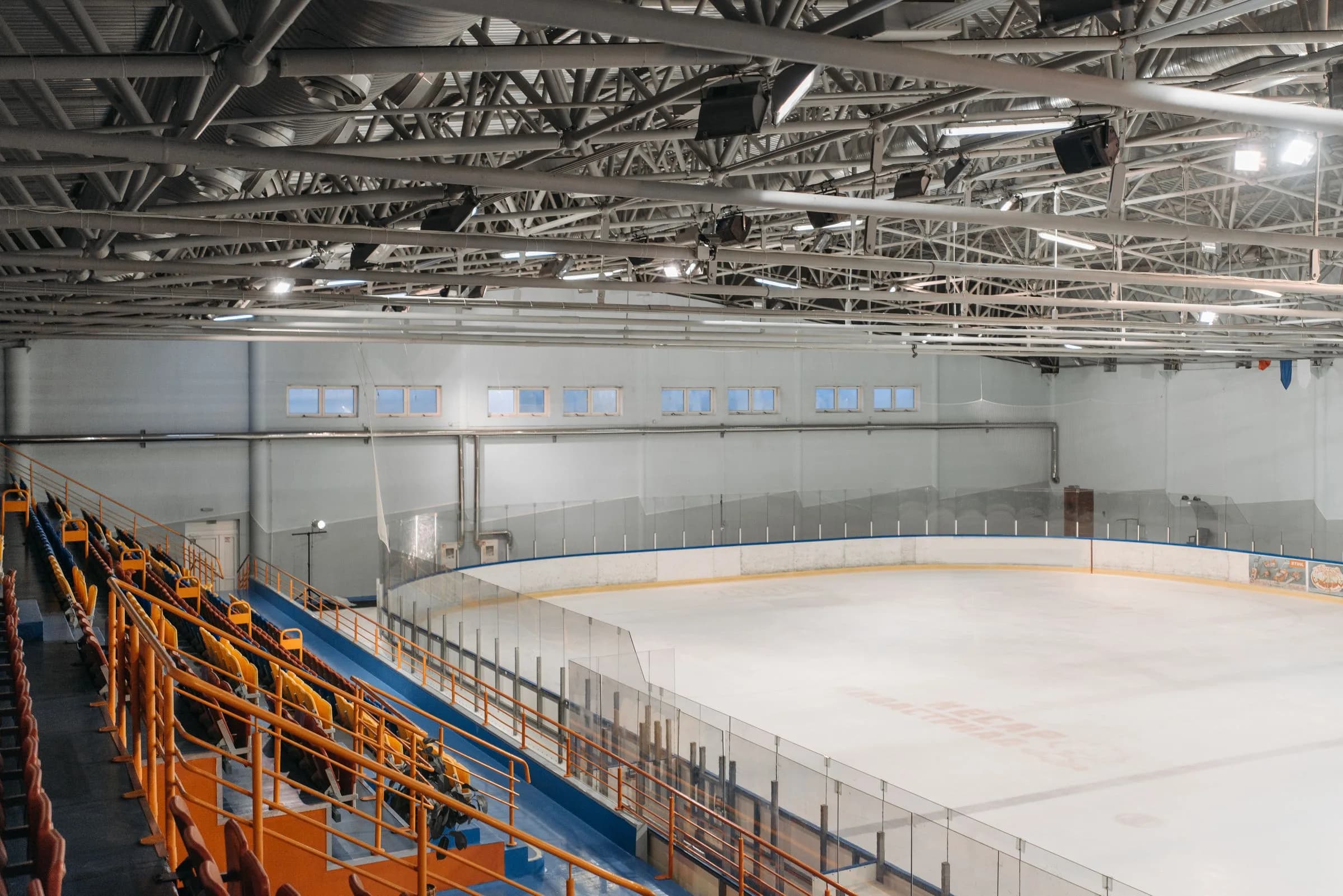 A wide view of an indoor ice rink with seating and overhead arena lights.
